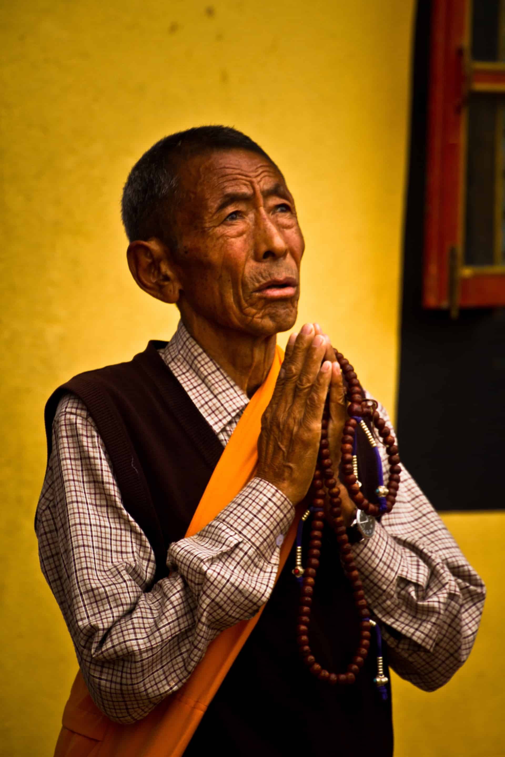 Elderly Tibetan man praying in Boudhanath Temple, Kathmandu, Nepal